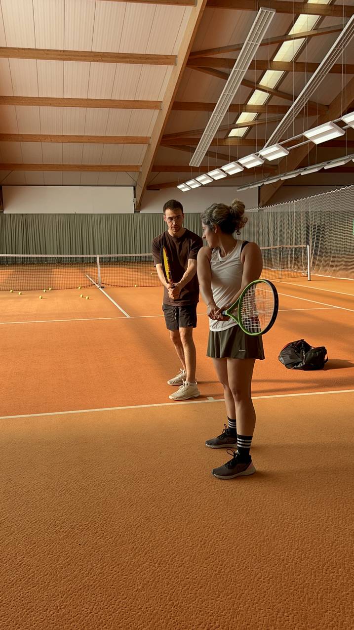 Coach teaching a student grip and stance one-on-one on a clay court